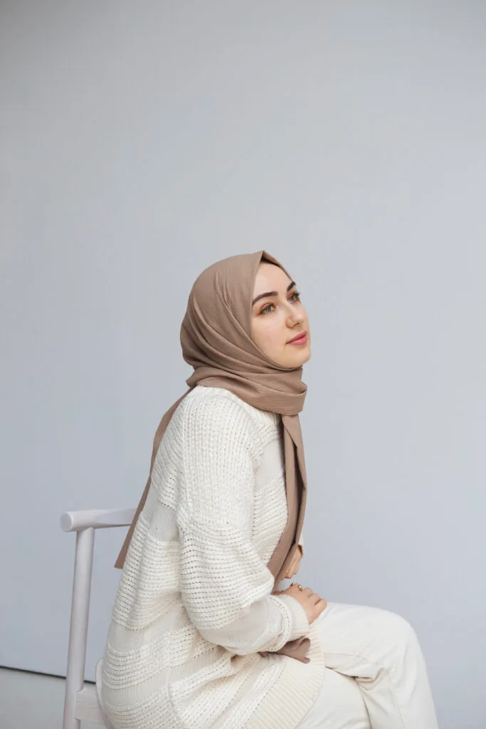 femme voilée avec un hijab en jersey premium beige, assise sur une chaise dans une salle blanche