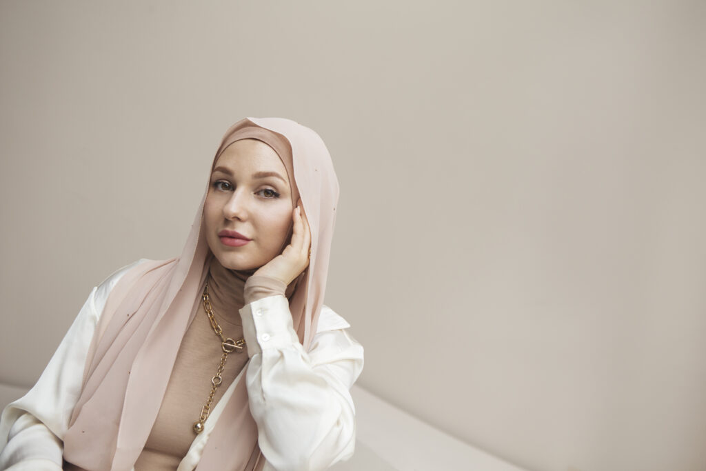 Femme voilée souriante, avec hijab nude rose clair assise