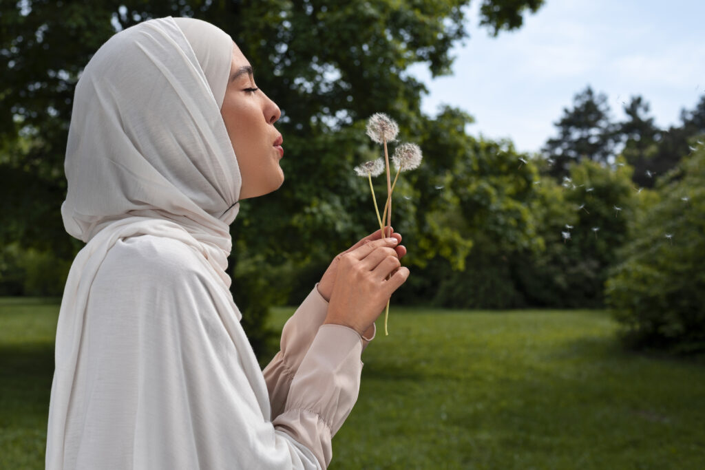 femme voilée hijab soufflant sur une fleur dans un jardin ensoleillé