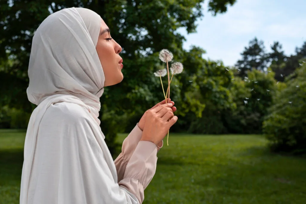 femme voilée hijab soufflant sur une fleur dans un jardin ensoleillé 